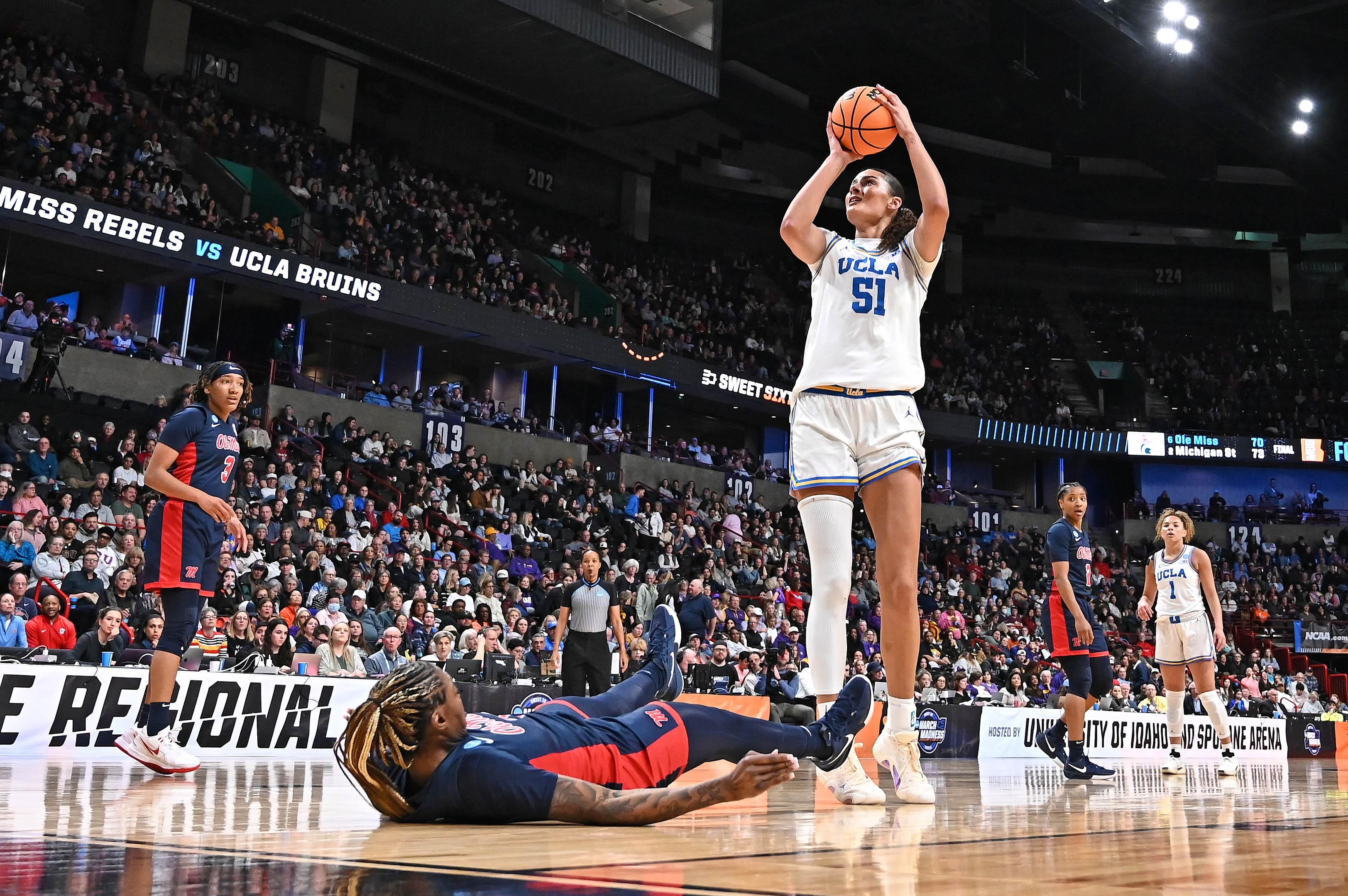 A woman's basketball player rises for a shot over a fallen defender.